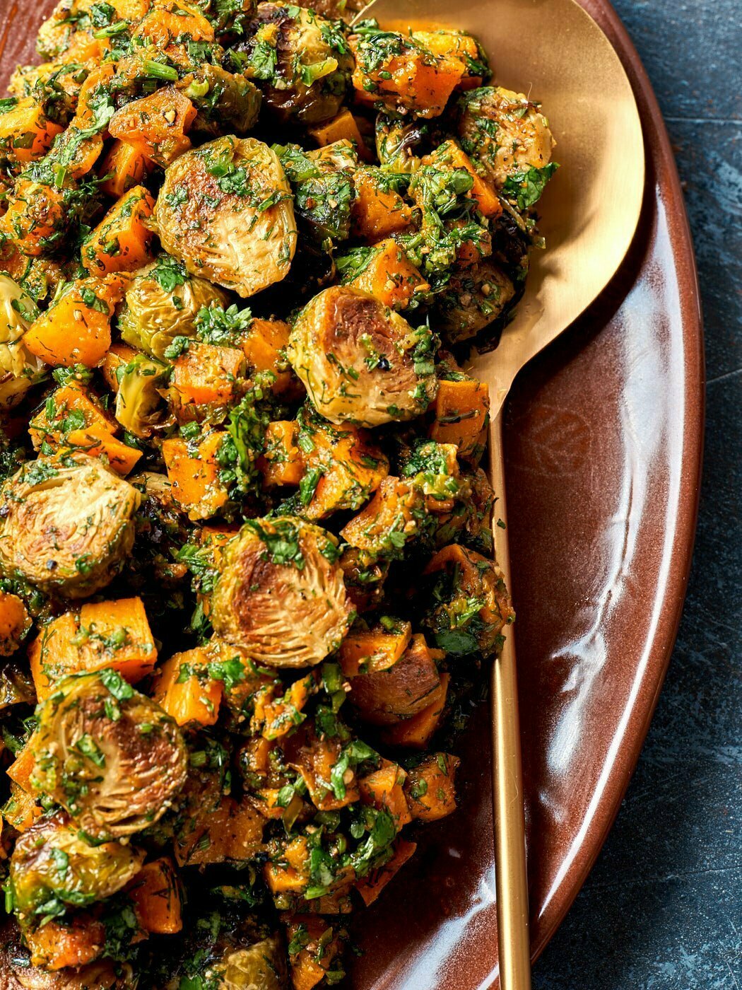 Crispy brussel sprouts and butternut squash topped with parsley sitting on a red platter.