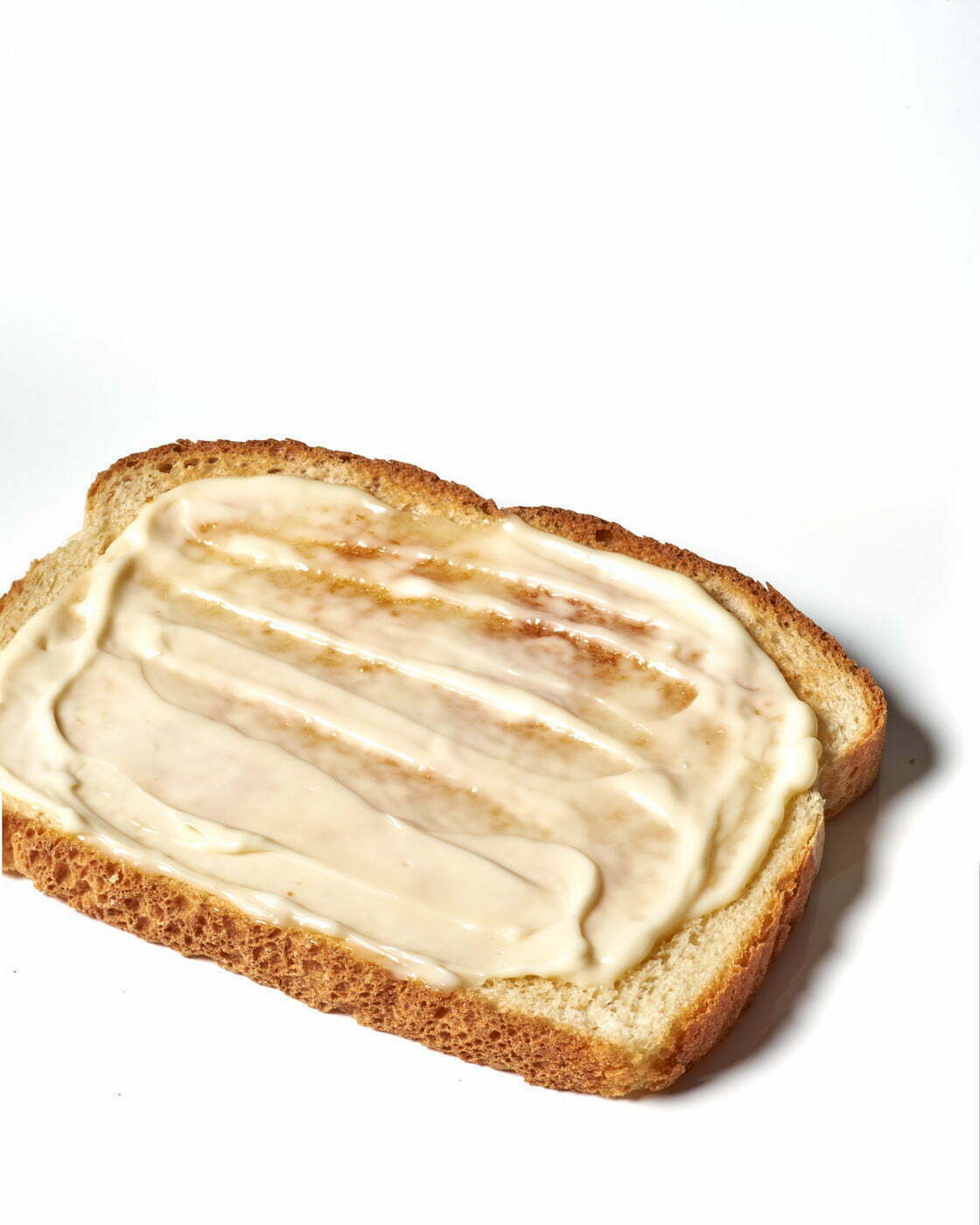 A single piece of white bread smeared with mayo on a white background