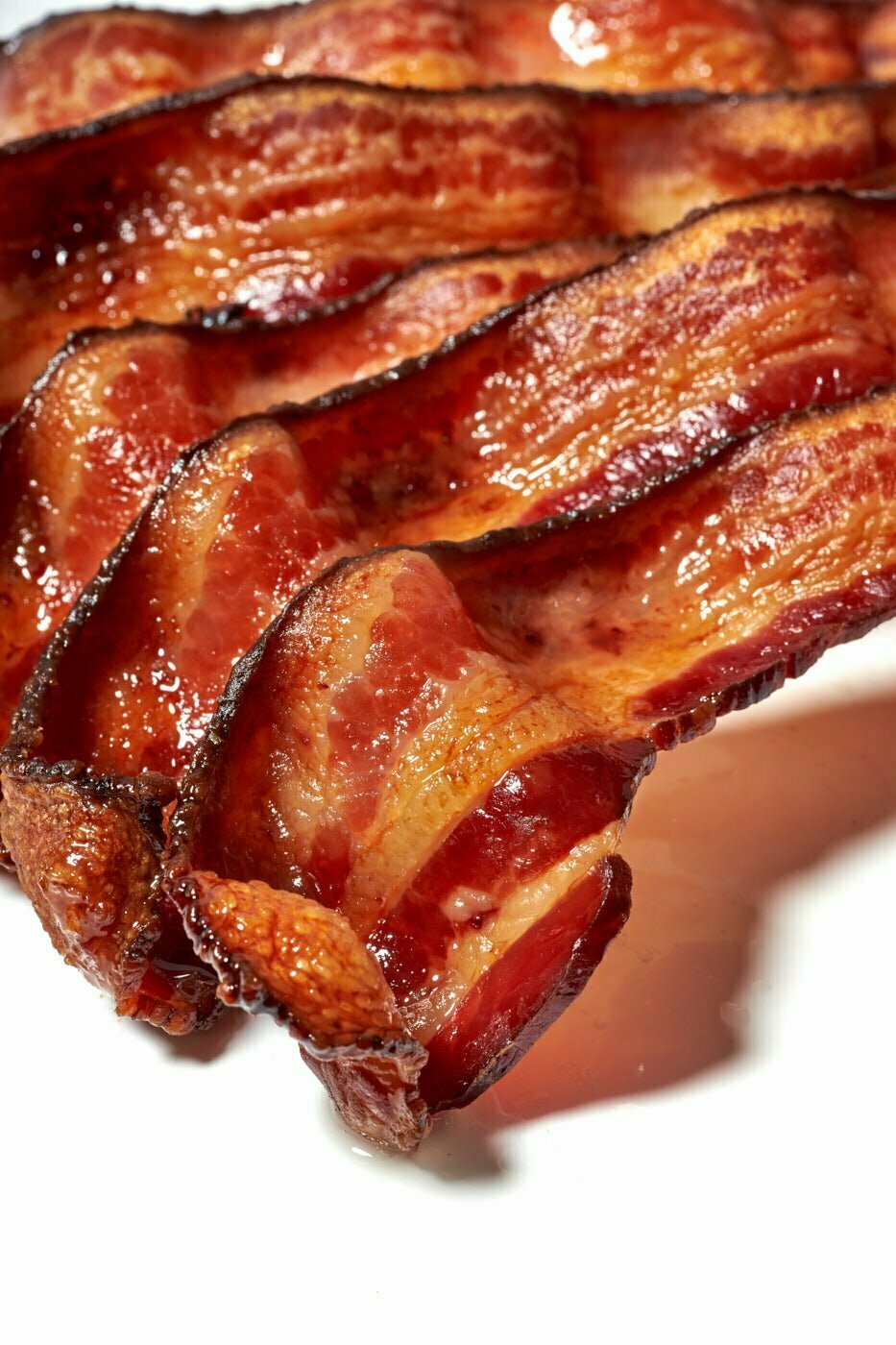 Cooked crispy bacon strips shingled on top of each other on white background