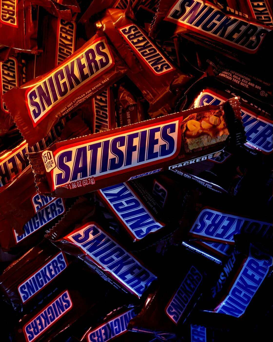 A full size Snickers candy bar still in wrapper sitting on top of mini Snickers candy bars also still in their wrappers.