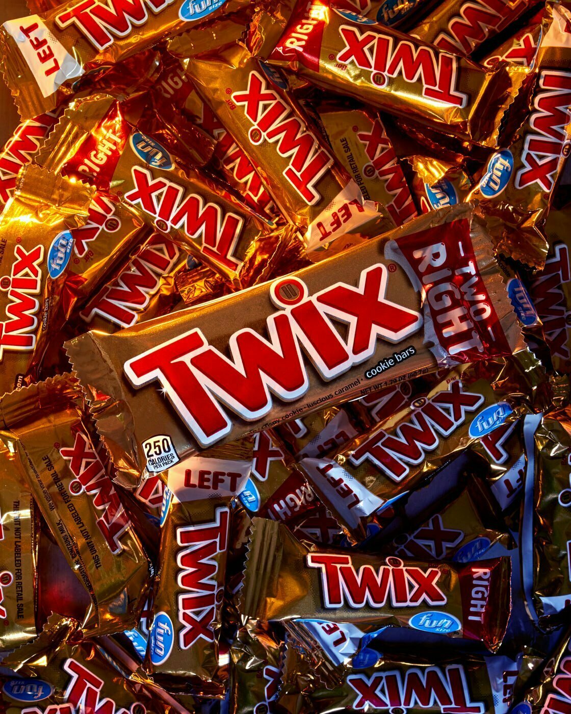 A full size Twix candy bar still in wrapper sitting on top of mini twix candy bars also still in their wrappers.